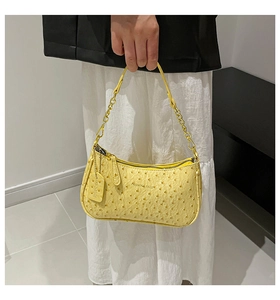 Detail of yellow baguette bag with ostrich texture, golden chain strap, and logo text