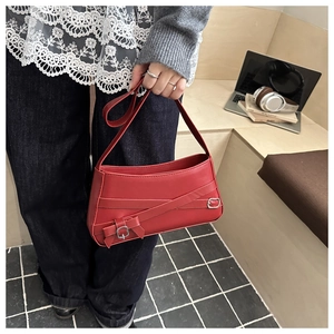 Detail of red leather shoulder bag with metallic buckle and bow decoration on wooden table