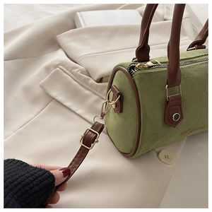 Detail of avocado green frosted Boston bag with brown handles on a beige blazer