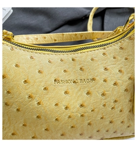 Close-up of yellow ostrich pattern leather crescent bag with golden zip and embossed text