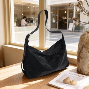 Minimalist black leather tote bag with silver buckle on a wooden table in a cafe