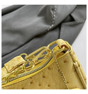 Close-up of golden hardware and ostrich leather texture on a yellow crescent bag
