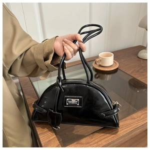 Detail of black patent leather bowling bag with silver plaque held by a model