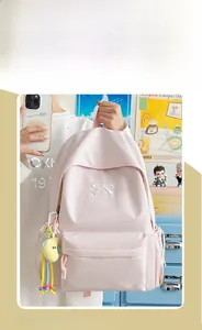 Detail of light pink student backpack with white bow embroidery and cute yellow charm