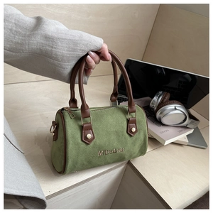 Close-up of green Boston bag with brown leather handles and brand embroidery details