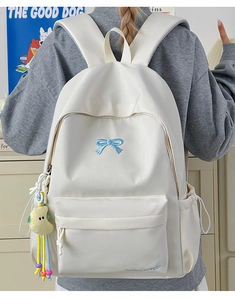 Detailed back view of white nylon backpack featuring a blue bow and moon plush charm