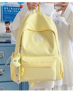 Detail of yellow nylon backpack featuring white bow embroidery and a moon plush keychain