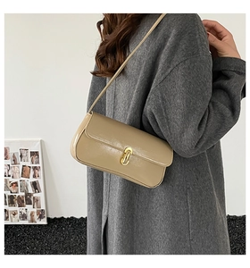 Close-up of beige baguette bag with gold metal buckle shown on model shoulder