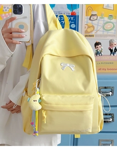Close-up of pale yellow canvas backpack with white bow embroidery and cute moon plush charm