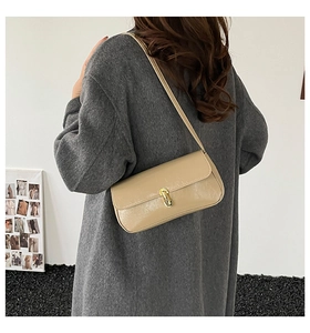 Close-up of beige glossy baguette bag with gold metal buckle shown on shoulder