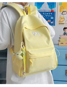 Close-up of yellow nylon backpack featuring white bow embroidery and moon plush pendant