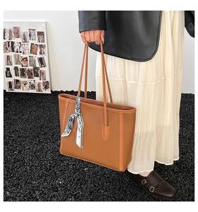 Detail of a large brown leather tote bag featuring long handles and decorative blue scarf