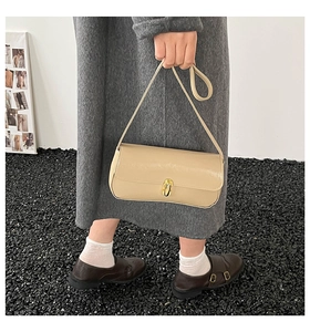 Detail view of a beige glossy leather baguette bag with a gold twist-lock closure