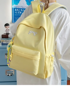 Detail of yellow nylon backpack featuring white bow embroidery and colorful bead charm
