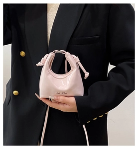 Detail of pink patent leather mini handbag with silver metal rings and logo on black suit
