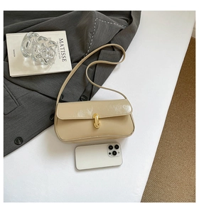 Détail macro du sac baguette beige brillant avec fermoir doré et livre d'art