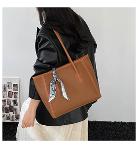 Detail of caramel brown pebble leather tote bag featuring a decorative floral scarf on handle