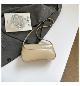 Détail d'un sac baguette en cuir beige chic porté avec un blazer gris et des livres