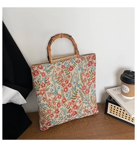 Detail of retro floral woven cotton tote bag featuring natural bamboo handles on a wooden table