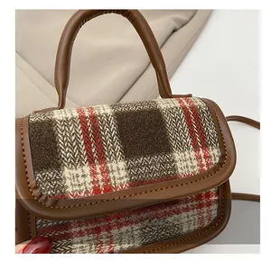 Gros plan sur la texture du tissu écossais rouge et marron et le liseré en cuir du sac
