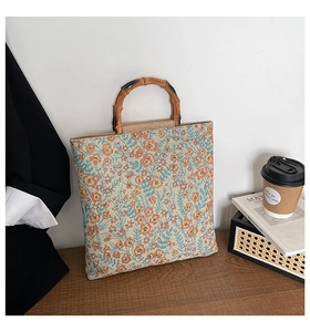 Detail of floral jacquard canvas tote with natural bamboo handles on a wooden table