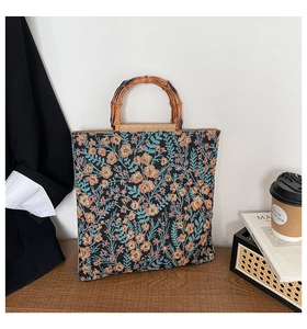Detail of vintage floral jacquard tote bag with natural bamboo handles on a wooden table