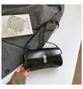 Détail du sac baguette noir brillant avec fermoir doré sur fond de blazer gris