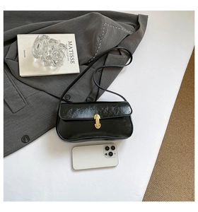 Détail du sac baguette noir brillant avec une boucle métallique dorée élégante
