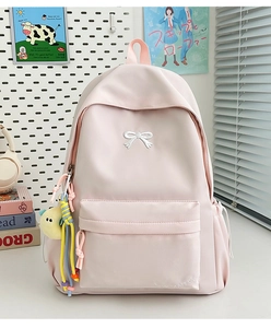 Close-up of light pink nylon backpack featuring bow embroidery and plush pendant