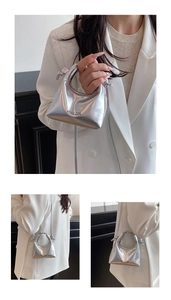 Detailed view of a silver metallic dumpling bag with thin crossbody strap and logo