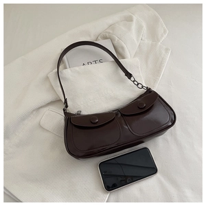 Détail d'un sac à bandoulière vintage marron foncé avec deux poches sur un blazer blanc