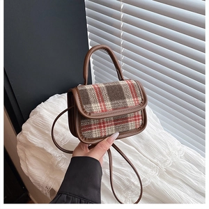 Detail of vintage plaid handbag with brown leather trim and handle on white fabric