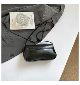 Détail d'un sac baguette noir brillant sur un bureau avec accessoires élégants