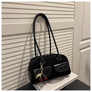 Detail of vintage black shoulder bag with dual pockets and cherry charm on books