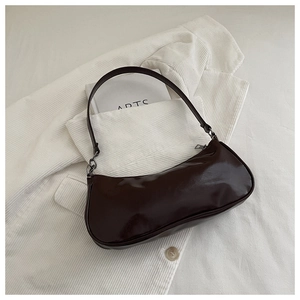 Gros plan du sac à bandoulière en cuir verni marron foncé sur texture de velours blanc