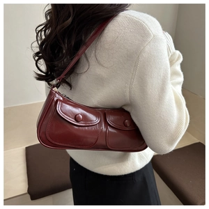 Détail du sac sous le bras en cuir verni bordeaux avec deux poches à rabat sur l'épaule