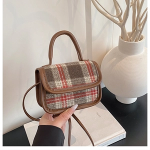 Detail shot of the vintage plaid tweed texture and brown leather trim on a shoulder bag