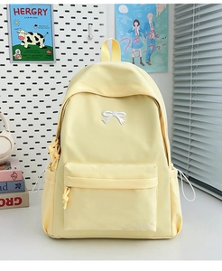 Detail of yellow nylon backpack featuring white bow embroidery and waterproof fabric