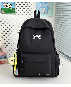 Detail of black nylon backpack with white bow embroidery and yellow plush charm accessory