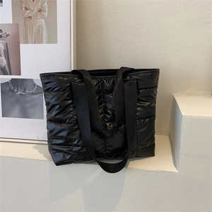 Quilted black puffer tote bag with glossy finish on a minimalist display stand