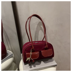Detail of burgundy suede tote bag with shiny leather pockets and a cherry charm