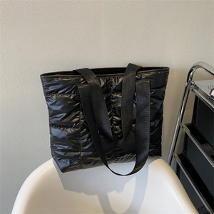 Modern black quilted tote bag with padded down-style fabric and wide straps on a chair