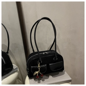 Detail of black suede baguette bag with leather front pockets and cherry charm on books