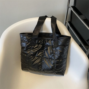 Black quilted puffer tote bag in glossy nylon fabric resting on a white minimalist chair