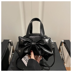 Détail d'un sac à main en cuir noir avec un grand nœud et des rivets en étoile