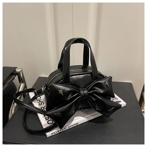 Détail d'un sac seau noir avec un nœud et des rivets étoiles sur un livre blanc