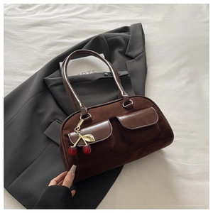 Detail of retro brown suede baguette bag featuring glossy leather pockets and cherry charm