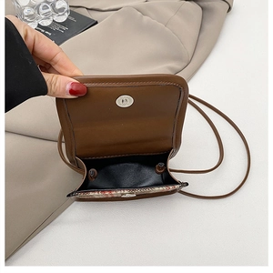 Close-up of brown leather crossbody bag with magnetic closure and plaid interior lining