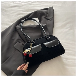 Detail of black suede baguette bag with leather pockets and red cherry metal charm on a suit