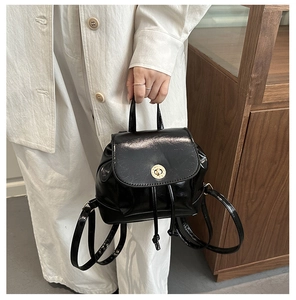 Detail of black glossy mini backpack featuring a gold twist lock and drawstring closure